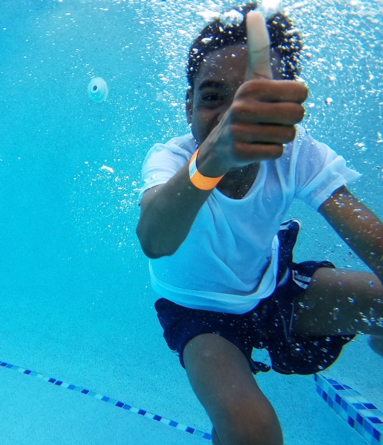 Child giving a thumbs up underwater in a swimming pool